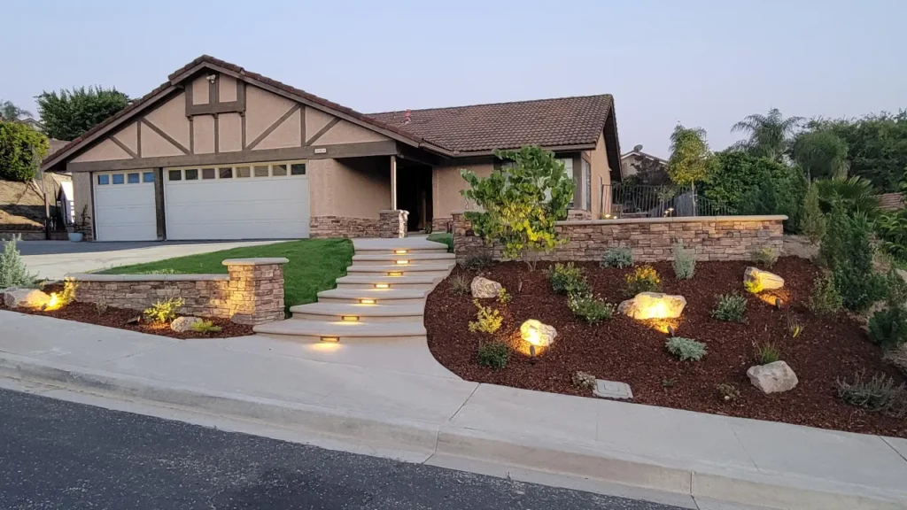 Front view of a single-story house with a three-car garage, curved lit steps, stone accents, and a landscaped yard.