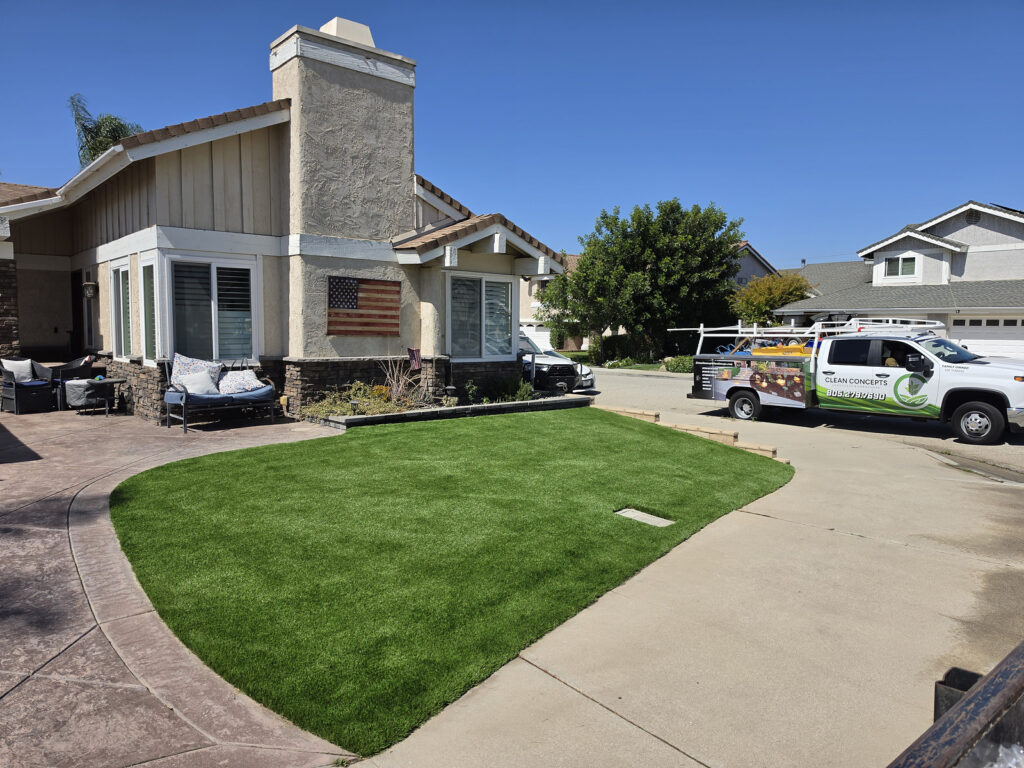 Front yard of a suburban house with green lawn and a patio seating area; a service van is parked in the driveway.